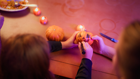 A small girl is painting pumpkin as a Halloween decoration with her mother in the living room at home.