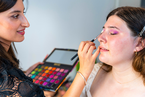 Makeup artist applying liquid tonal foundation on the eye of the woman in make up room