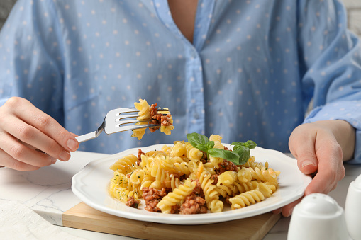 Woman eating delicious pasta with minced meat and basil at white table, closeup