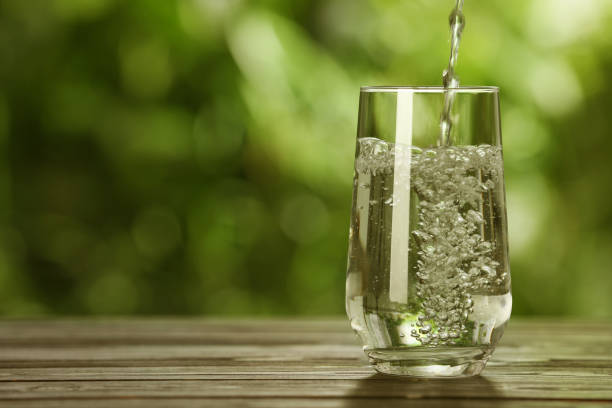 istock Pouring water into glass on wooden table outdoors, space for text 1678475191