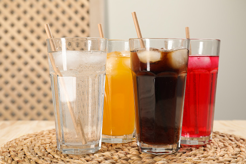Glasses of different refreshing soda water with ice cubes and straws on wooden table