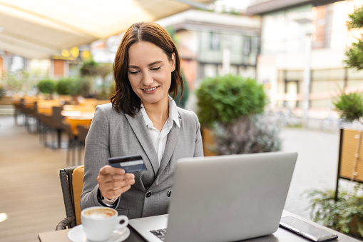 Young smiling woman e-banking over laptop while having coffee break in a cafe