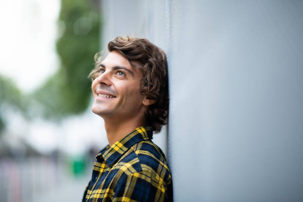 istock Young man leaning against gray wall looking up and smiling outside 1678479369