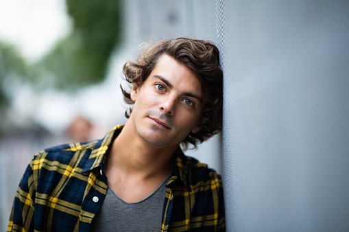 Close up portrait of handsome young man leaning against gray wall and staring at camera