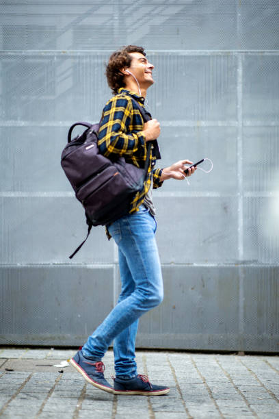 istock Handsome young guy with bag walking outside with cellphone and earphones 1678480075