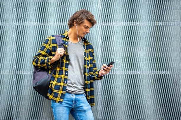 istock Handsome young man standing by grey wall with mobile phone and earphones 1678480093