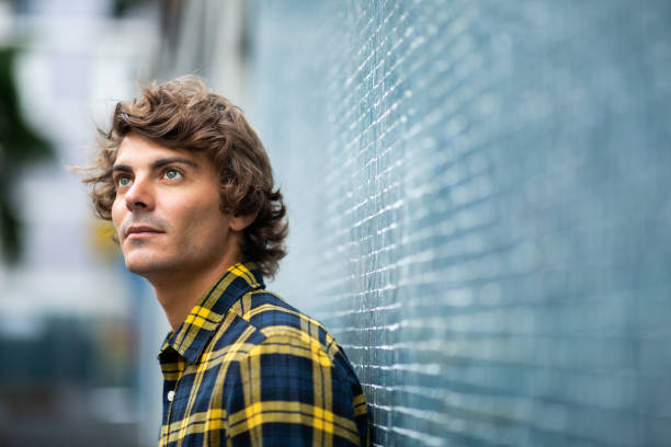 istock Thoughtful young man leaning against gray wall looking away 1678480102