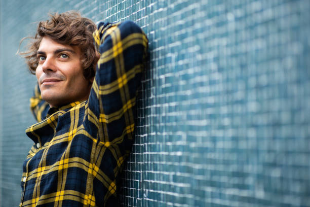 istock Thoughtful young man leaning against gray wall with hands behind head 1678480228