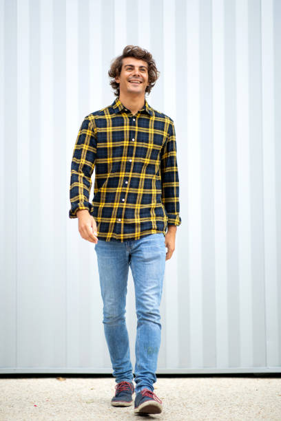 Handsome young man in checked shirt and denim jeans walking outside