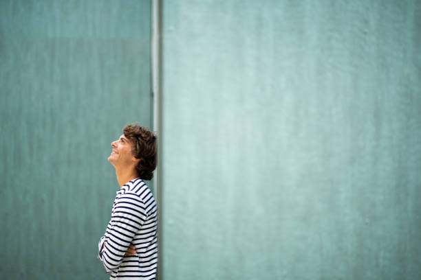 Side portrait of happy young man leaning to green wall looking up and smiling
