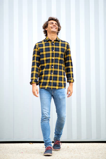 istock Smiling young guy in checked shirt and denim jeans walking outside 1678482825