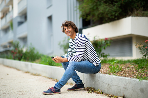 Portrait of attractive young man sitting outside with cell phone in city