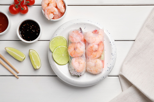 Delicious spring rolls with shrimps wrapped in rice paper served on white wooden table, flat lay