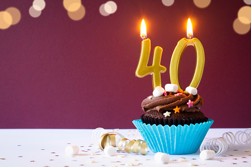 Chocolate buttercream cupcake with chocolate icing, sprinkles and gold 40th birthday candles. 
Shot  on a maroon background with defocused lights.