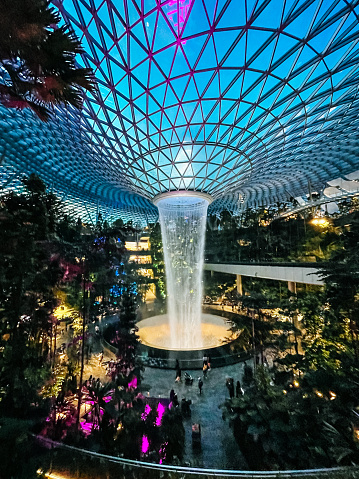 Jewel Changi Airport, Singapore - 11th October, 2022: Night view  of illuminated Rain Vortex inside the Jewel area at Changi Airport. It's the world's tallest waterfall at 130 ft in height and surrounded by a four-storey terraced forest. The Jewel complex and waterfall was designed by Moshe Safdie.