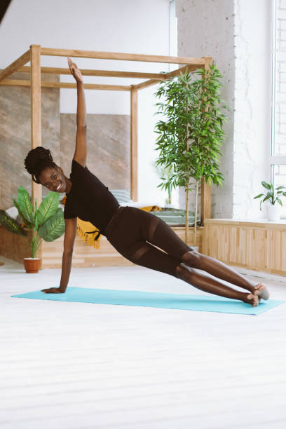 istock Vertical smiling multicultural woman do yoga exercises on mat. Practicing Vasisthasana side plank. Keep balance as coach 1678553779