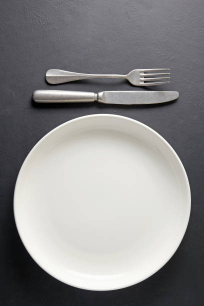 istock White ceramic plate and cutlery fork and knife on a black concrete background. Template for displaying food on menu 1678611372