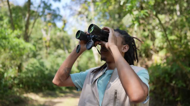 Young man using binoculars during hiking on forest