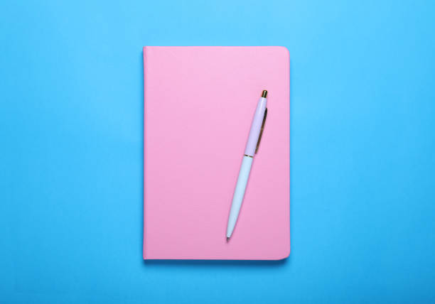 istock Closed pink notebook and pen on light blue background, top view 1678639089