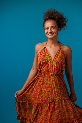 Portrait of charming young woman standing against blue background, looking at camera and smiling joyfully.