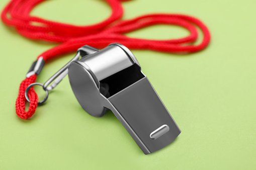 One metal whistle with red cord on light green background, closeup