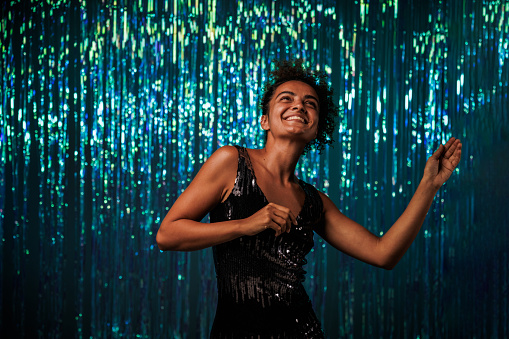Portrait of excited young woman dancing against blue iridescent fringe curtain during a fun party.