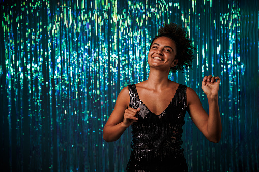 Portrait of excited young woman dancing against blue iridescent fringe curtain during a fun party.