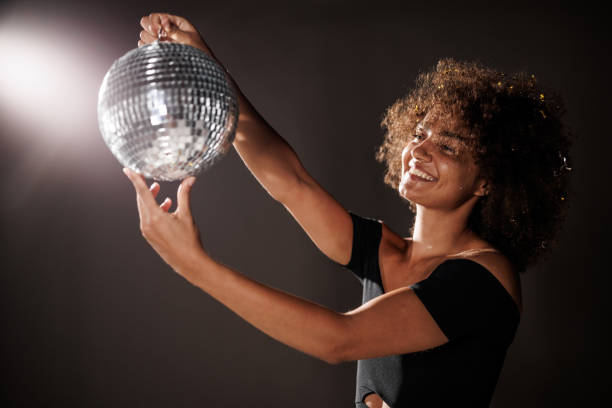 Young woman holding a disco ball against dark gray background