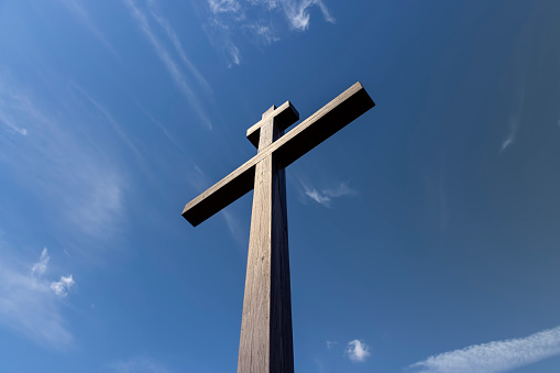 an old wooden Orthodox cross against a blue sky with clouds, part of a wooden religious cross of the Orthodox denomination
