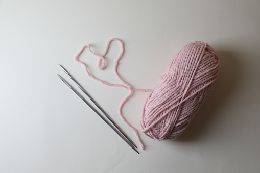 Soft pink yarn and metal knitting needles on light background, top view