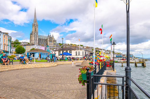 Saint Colman's Cathedral can be seen rising above the colorful Irish seaside town's waterfront promenaded and boardwalk at Cobh, County Cork, Ireland