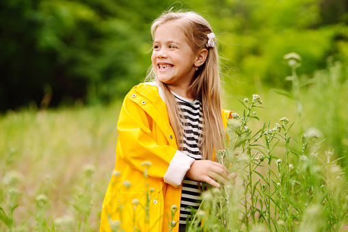 A little girl in a yellow coat is having fun, collecting wildflowers in the park. The child explores nature. The concept of childhood, joy.