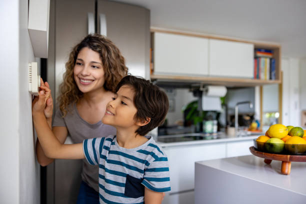 Mother and son adjusting the temperature of their house Happy mother and son adjusting the temperature of their house using a thermostat and smiling - lifestyle concepts air conditioner family stock pictures, royalty-free photos & images
