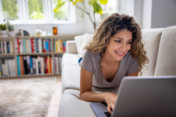 istock Happy woman working at home on her laptop while lying on the couch 1678741961