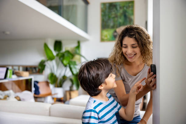Mother and son at home adjusting the temperature using a smart thermostat Happy mother and son at home adjusting the temperature using a smart thermostat and smiling - lifestyle concepts air conditioner family stock pictures, royalty-free photos & images