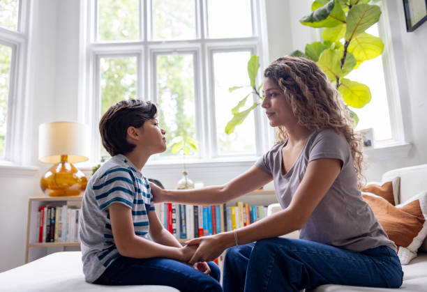 Mother comforting her son while talking at home Loving mother comforting her son while talking at home - lifestyle concepts worried mom with kids stock pictures, royalty-free photos & images