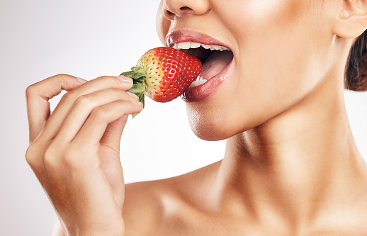 Woman, strawberry and mouth for eating, studio and healthy with nutrition, diet and bite by white background. Girl, model and fruit for wellness, detox or cosmetics with detox, vitamin or vegan meal
