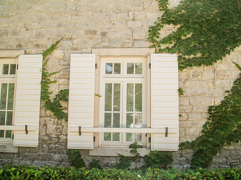 White stone house wall with window with green ivy