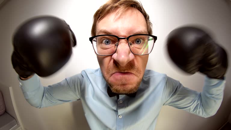 Fisheye portrait of nerdy angry man with boxing gloves posing at camera.