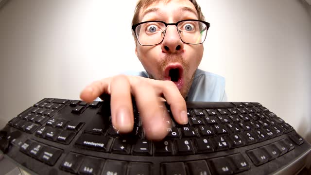Fisheye portrait of crazy nerd with glasses typing keyboard, looking at camera