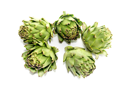 Uncooked organic purple artichokes with lemon slices on a frying pan. Rustic style on black surface. Dark photography style with copy space