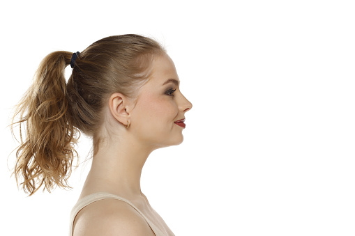 Profile, side view of beautiful smiling blonde woman with tied hait on a white studio background
