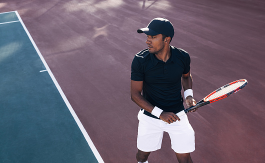 Tennis player in sportswear and a cap standing on a hard court preparing to receive the serve. Tennis player during a tennis match.
