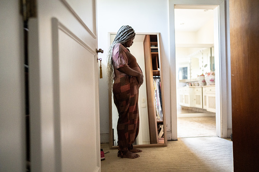 Pregnant woman looking at herself in the mirror while touching her abdomen at home