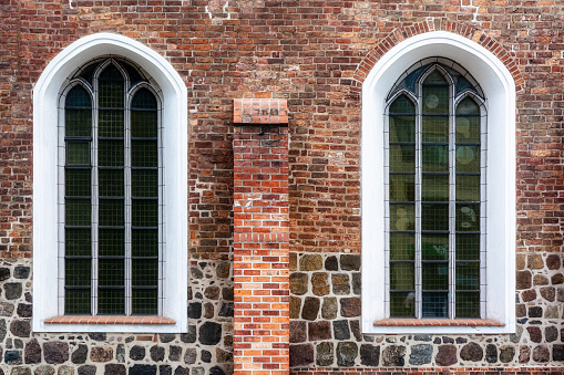 Two arched windows with metal bars and white edging on an old red brick wall. From the Windows of the world series.