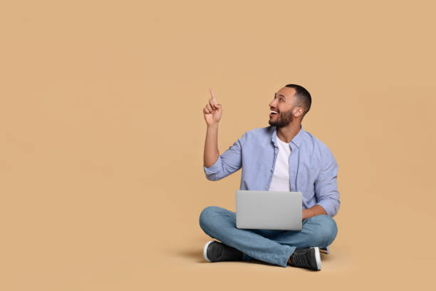 istock Smiling young man with laptop on beige background, space for text 1678873822