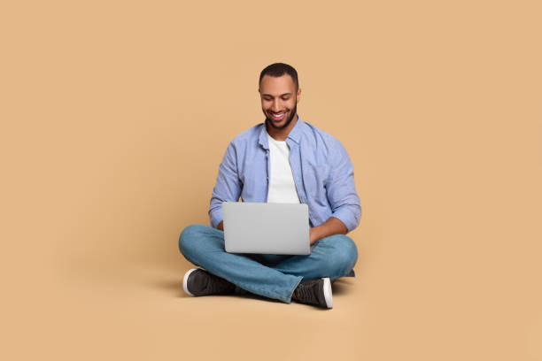 istock Smiling young man working with laptop on beige background 1678874065