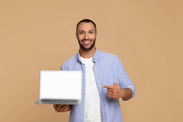istock Smiling young man showing laptop on beige background 1678874339