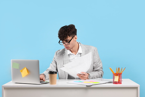 Young man working at white table on light blue background. Deadline concept