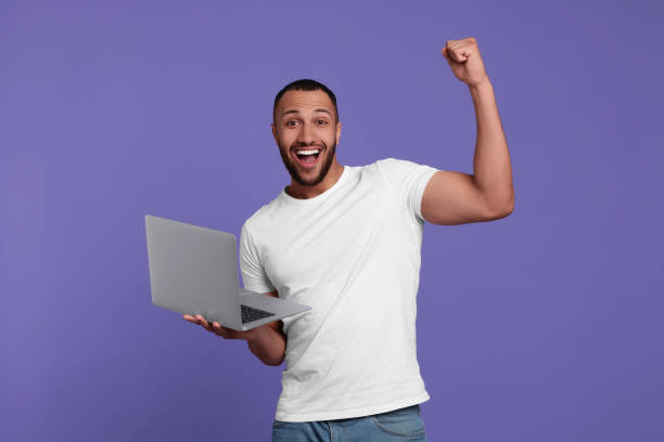 istock Happy young man with laptop on lilac background 1678874835